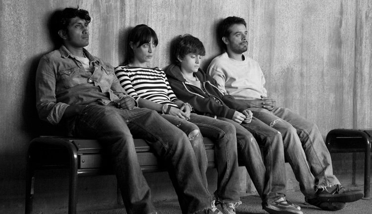 Imagen en blanco y negro de los personajes de la pelicula Güeros sentados en una banca  con miradas tristes.